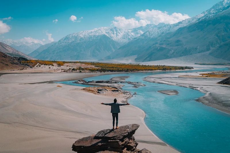 homme posé sur un rocher face à la montagne et à la rivière invitant à un voyage nature