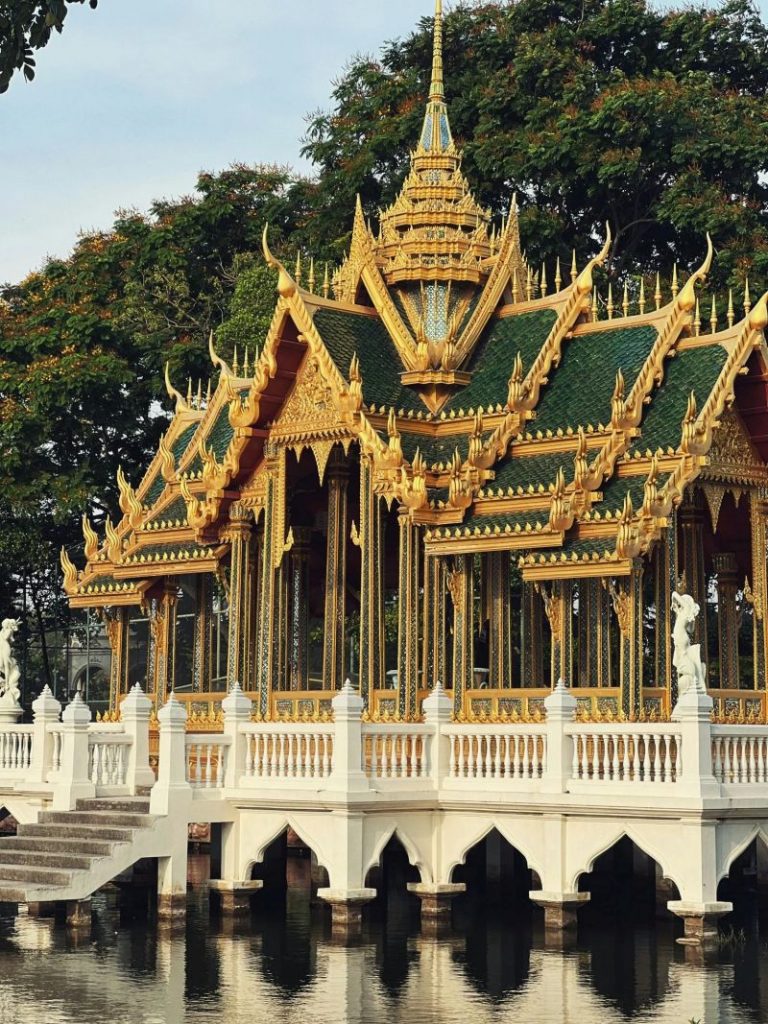 Magnifique architecture de pavillon thaïlandais avec des détails complexes reflétés dans des eaux tranquilles, entouré d'une verdure luxuriante.