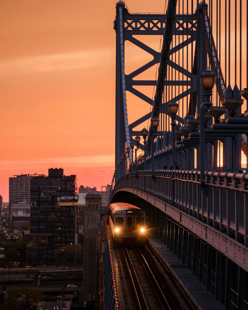 Train traversant le pont Benjamin Franklin au coucher du soleil à Philadelphie, présentant des vues sur le paysage urbain.